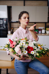 Portrait beautiful woman holding a flower composition posing on white kitchen at home. Florist presenting a basket with colorful flowers