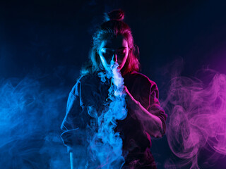 Girl smokes a VAPE on a dark background. Woman lets out clouds of smoke from an electronic...