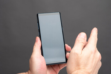 A man uses a smartphone. The man touches the touch screen with his finger. Men's hands with a smartphone on a gray background. A mobile phone with space for your text on the screen.
