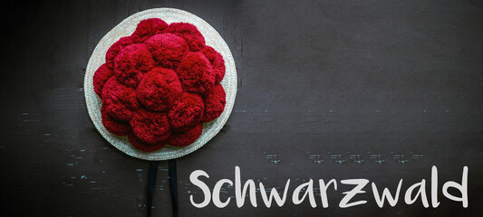 Roter Bollenhut Tracht aus dem Schwarzwald - isoliert auf schwarzer rustikaler Holzwand / Textur / Hintergrund
 - obrazy, fototapety, plakaty