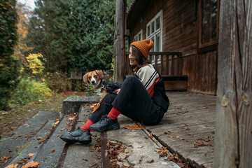 stylish young woman with a cute dog near the old cozy house