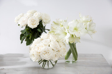 White roses, lily, in round vases with two cups of coffee on the table for a special occasion as a kitchen decoration.