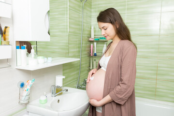 Young pregnant woman applying anti-stretch marks cream to the abdomen in the morning in the...