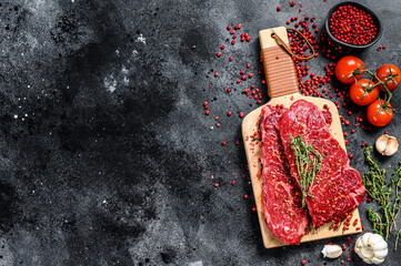Denver steak on a cutting board. Marble raw beef meat. Black background. Top view. Copy space