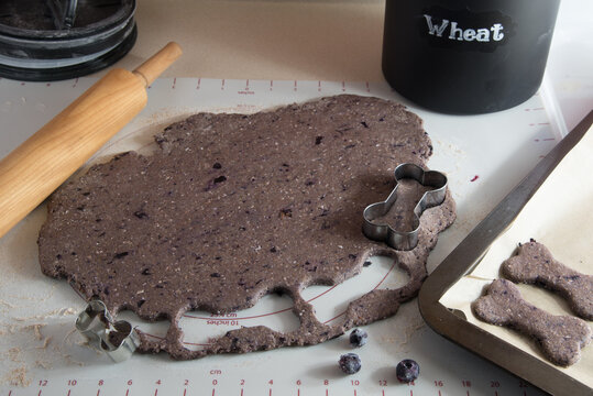 Dough on pastry mat. Cutting out bone shaped blueberry dog treats. Healthy snacks for your favorite pet.