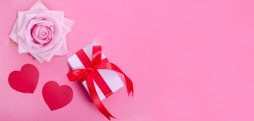 Valentine's Day banner background. Pink rose with red hearts and a gift on a pink background with copy space.