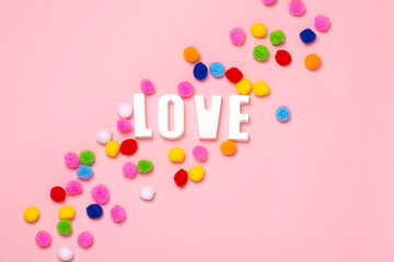 Bright creative card for Valentine's Day. The inscription Love in multi-colored pom-poms on a pink background. Valentines day creative concept