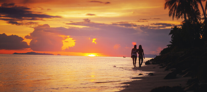 Silhouette of romantic couple on a tropical beach walking on the sand watching the sunset over the sea