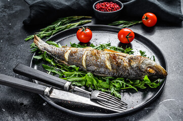 BBQ sea Bass fish with arugula, fried sea bass. Black background. Top view