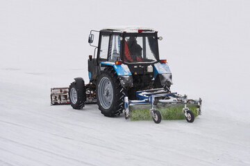 tractor with a snow plow and a mechanical sweeper moves on a snowy background