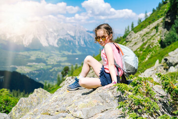 Naklejka premium Children hiking on beautiful summer day in alps mountains Austria, resting on rock and admire amazing view to mountain peaks. Active family vacation leisure with kids. Outdoor fun and healthy activity