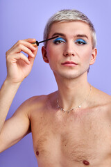 transgender man applying mascara on eyelashes against color background, portrait. gay, lgbt