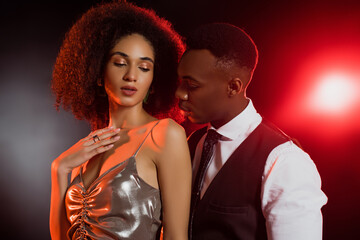 African american man in suit looking at elegant woman on black