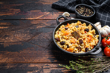 Pilaf in a pan. Central Asian cuisine Plov.  Dark wooden background. Top view. Copy space