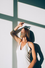 Naklejka premium Pandemic fashion. Female elegance. New normal lifestyle. Beautiful sensual woman in classic white dress designer golden chain turquoise beads face mask posing on sunlight.