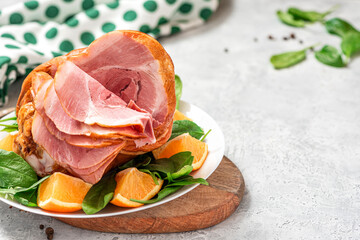 Sliced ham in a plate close-up. Baked pork ham with oranges and spinach on a gray concrete background. Free space for text