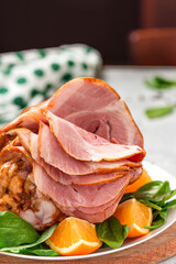 Sliced ham in a plate close-up. Baked pork ham with oranges and spinach on a gray concrete background.