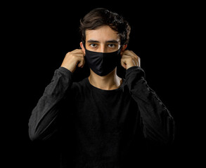 Fototapeta na wymiar Young man wearing black face mask. Pandemic coronavirus covid-19 quarantine period concept. Black background studio