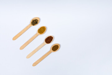 Various spice seeds in wooden spoons on a white background diagonally. Seeds of beet, mustard, lettuce, rukla, on a white background. Place for an inscription. View from above.