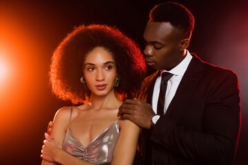 african american man in suit hugging curly woman in dress on black