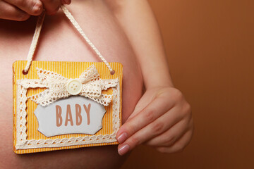 A pregnant woman holds a sign next to her belly on a yellow background