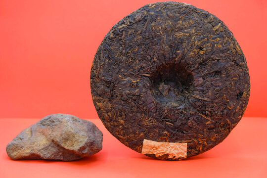 Round flat disc of puer tea isolated on a red background. Pressed Chinese fermented Pu-erh tea. Red mountain stone soil. Copy space. Mockup. 