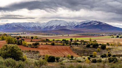 Green landscape with snowy mountains and dramatic sky in Somosierra Madrid.
