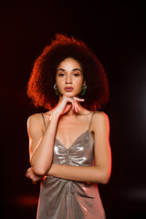 curly african american woman in dress looking at camera on black