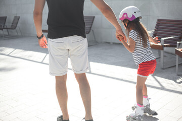 Parent teaching the kid rollerblading. The girl dressed protective helmet and rollers for skating....