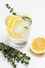Refreshing lemon drink with ice and sprig of thyme. Slice of lemon and sprig of thyme on table