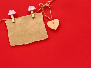 Valentines day mockup. A piece of brown craft paper pinned to the rope with pink clothespins. Wooden heart. Red background.