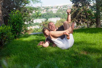 Fototapeta premium Happy family laughing in green grass of the park. Father plays with daughter. People have fun
