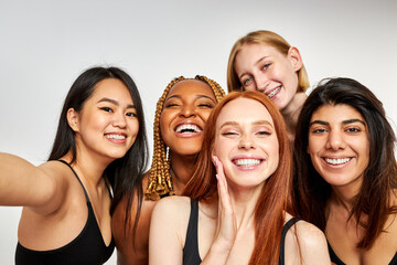 five smiling laughing beautiful women in bodysuit standing together, having fun and talking selfie looking at camera, isolated on white studio background