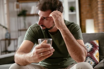 Muurstickers Depression man drinking alcohol at home. Lonely man is addicted of alcohol. © JustLife
