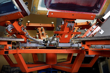 Print screening apparatus. serigraphy production. printing images on t-shirts by silkscreen method in a design studio.
