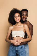 joyful african american woman and man smiling while hugging on beige