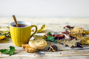 Autumn tea. Yellow cup of tea, homemade cookies surrounded by autumn leaves, a scarf, pumpkins and apples on a wooden table, copy space
Cozy style