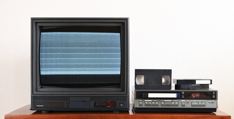 An old black vintage TV with noise and interference on the screen stands next to the VCR against...