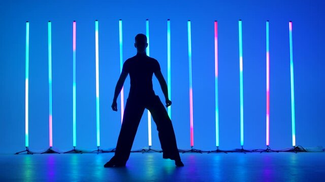 Ballroom dancer solo performance in a dark studio. Dark silhouette of a dancer against the background of bright multicolored neon tubes. Slow motion.