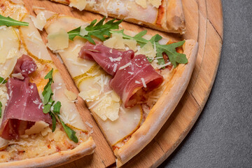 Italian pizza with sliced prosciutto ham, cheese, and fresh green rocket leaves closeup