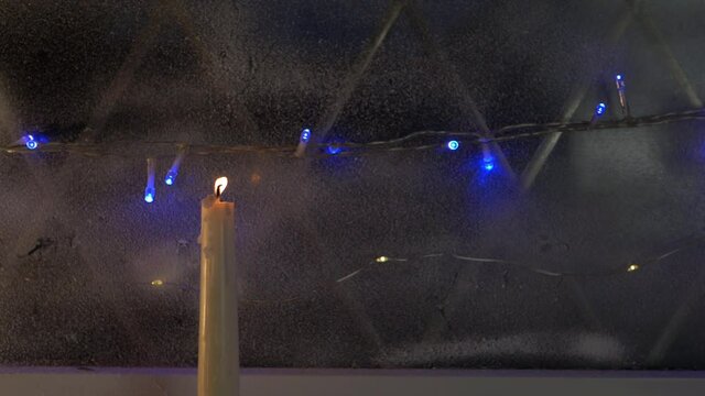 Candle burning in winter window scene with Christmas lights
