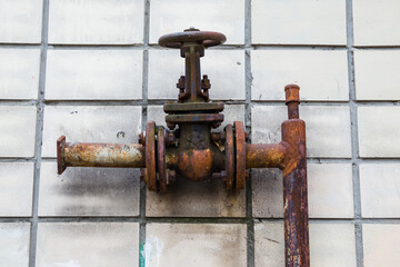 Old fire pipe system closeup fire hydrant detail. Rusty fire hydrant on the background of old tiles on the wall