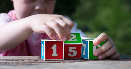 Children's hands hold learning cubes with numbers. Initial training in counting.
