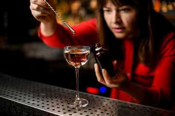 glass with liquid stands on bar and bartender adds ingredient to it