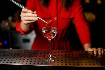 front view of wineglass which woman decorates with branch of plant using tweezers