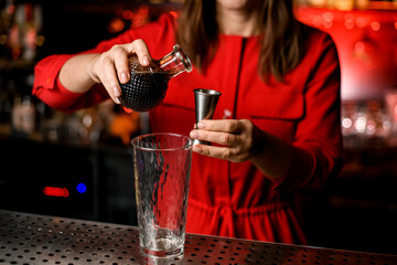 close-up on hands of woman holding metal jigger and crystal decanter of wine