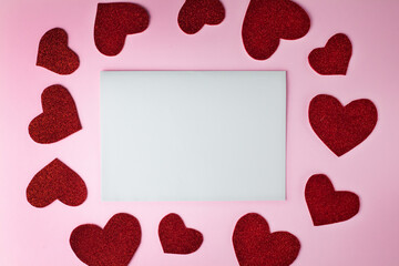 Blank sheet of paper with copy space to write your own text, red paper hearts on the pink background. Congratulation concept for Valentine's day, birthday. Place for text.