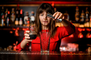 glass stands on bar and female bartender pours drink from jigger into it
