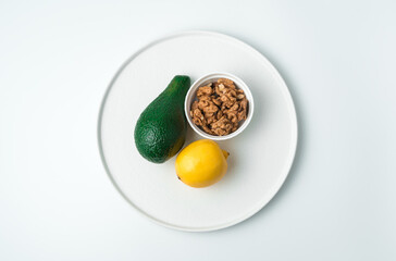 Flat white plate with avocado and lemon and walnuts on a white background. Top view with space to copy. The concept of healthy eating.