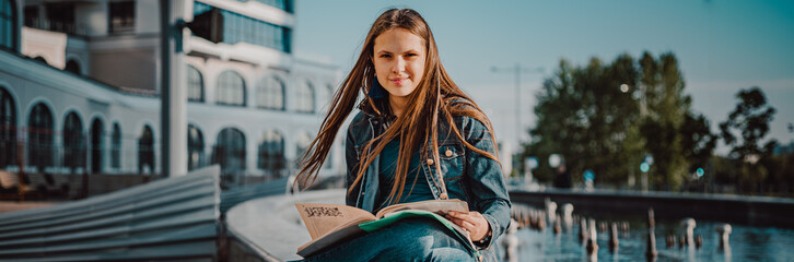 Back to school student teenager girl reads a textbook. Outdoor portrait of young teenager brunette...